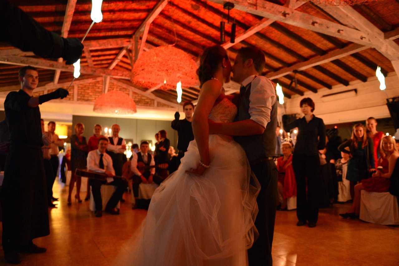 The bride and groom share a kiss on the dance floor while guests watch and a performer holds fire.