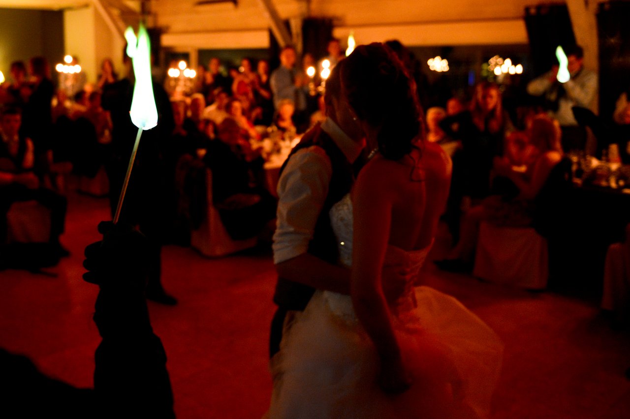 The bride and groom share a dance at their wedding reception, surrounded by guests holding glowing torches.