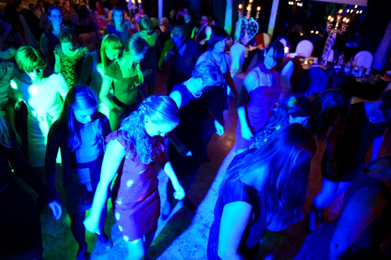 Wedding guests dancing in a dimly lit reception area with colorful lighting.