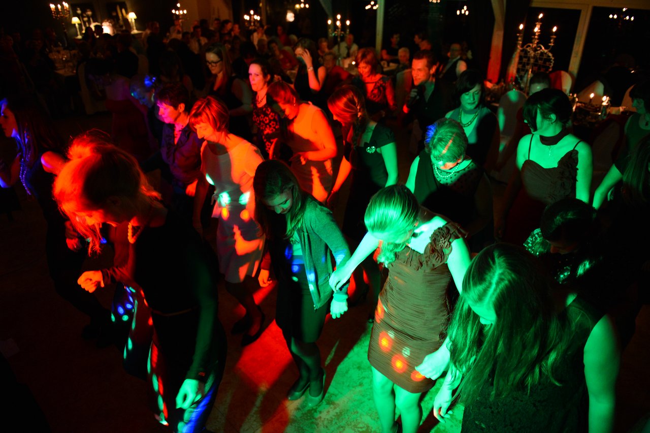 A group of wedding guests dance together under colorful lights at the reception.