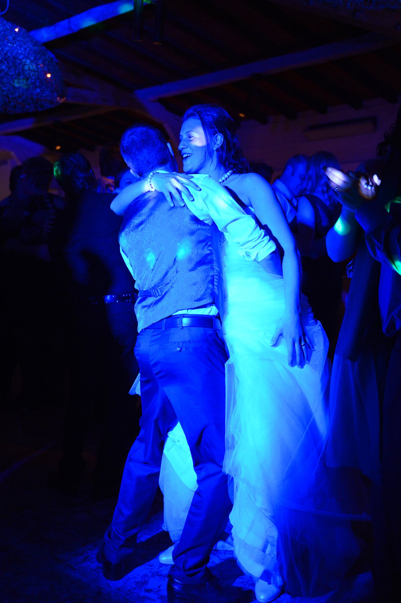 A bride and groom embrace and dance together at their wedding reception, surrounded by guests.