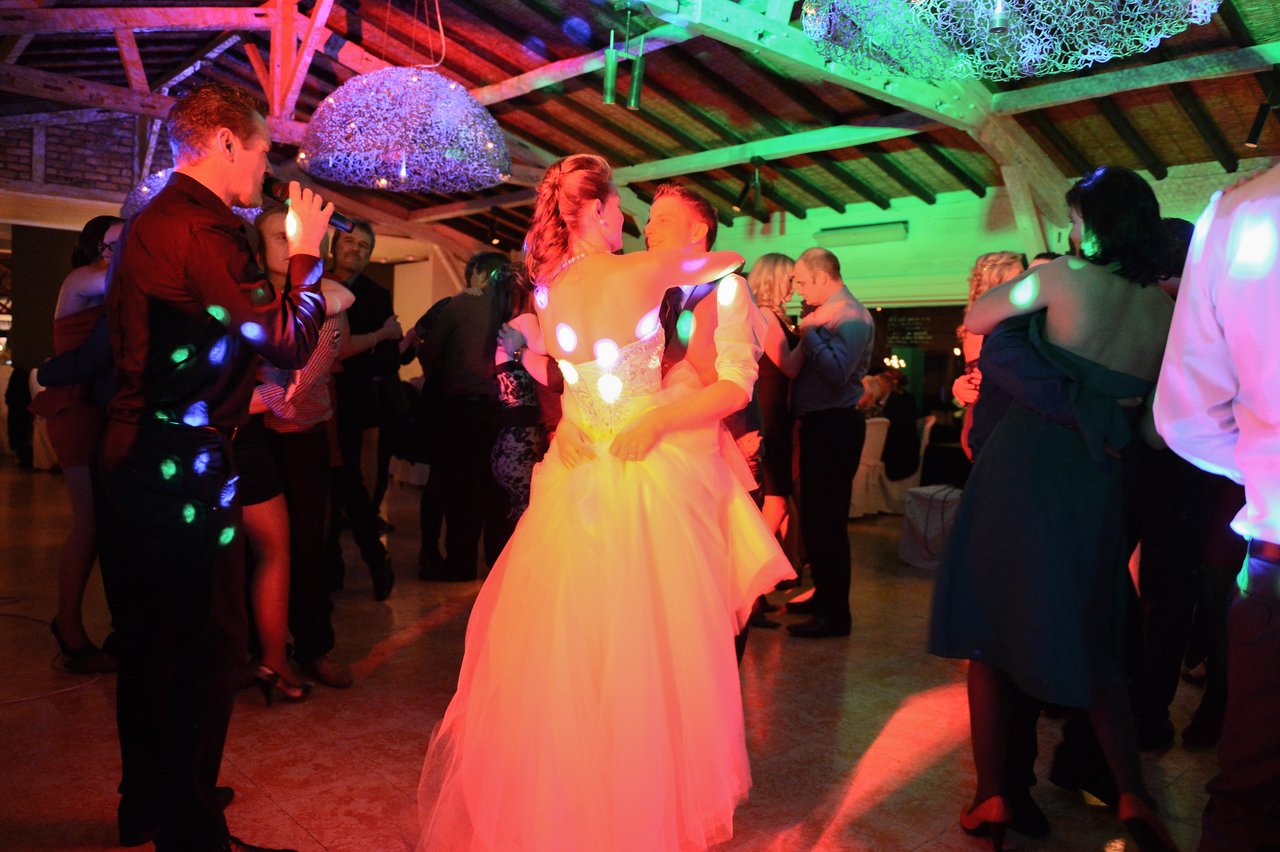 The bride and groom dance together at their wedding reception, surrounded by guests and colorful lights.