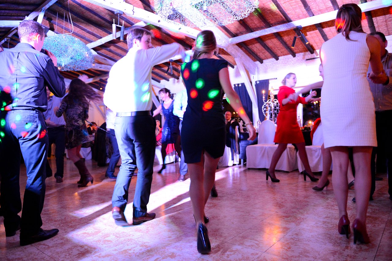 Wedding guests dance under colorful lights at a reception, dressed in formal attire and enjoying the celebration.
