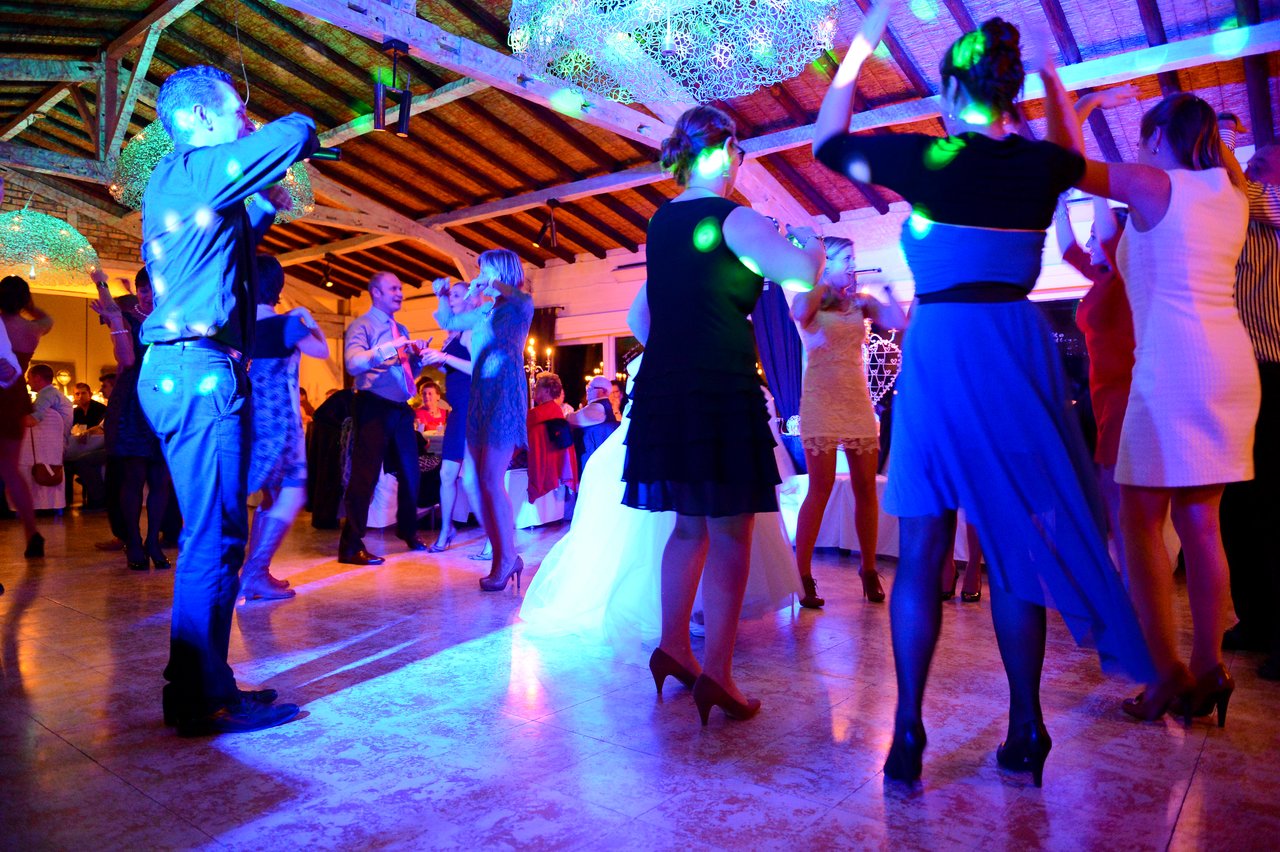 Wedding guests dance under colorful lights, with the bride in a white dress joining the celebration.