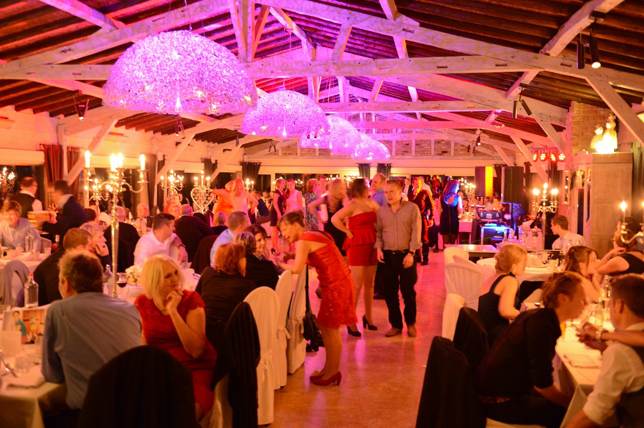 Guests are dining, talking, and dancing at a wedding reception in a warmly lit venue with festive decorations.