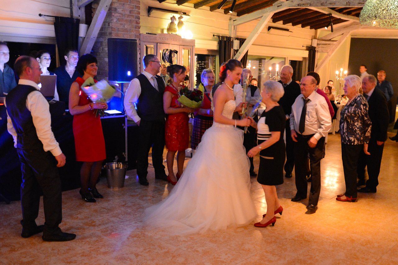 The bride in a white gown receives flowers from a guest while surrounded by family and friends at the wedding.