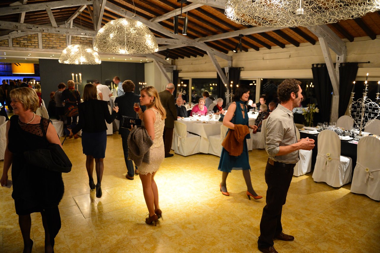 Guests mingle and chat at a wedding reception in a warmly lit venue with decorated tables and chairs.