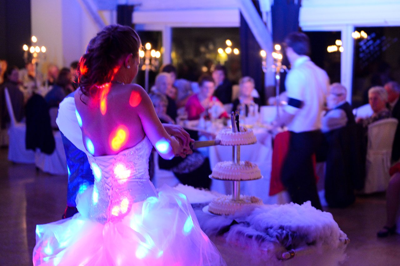 A bride in a white dress prepares to cut a tiered wedding cake at a reception with guests watching.