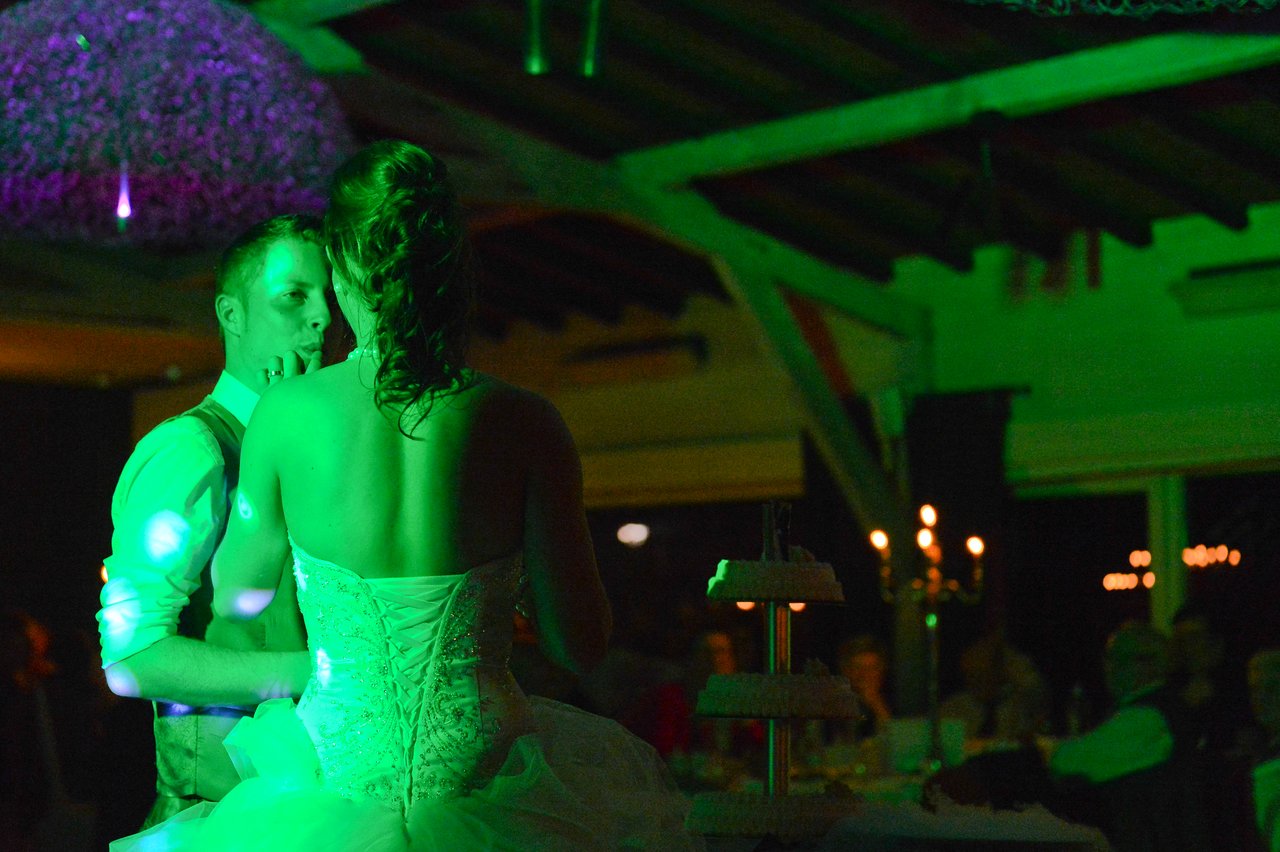 A bride and groom share a dance at their wedding reception, with a cake stand visible nearby.