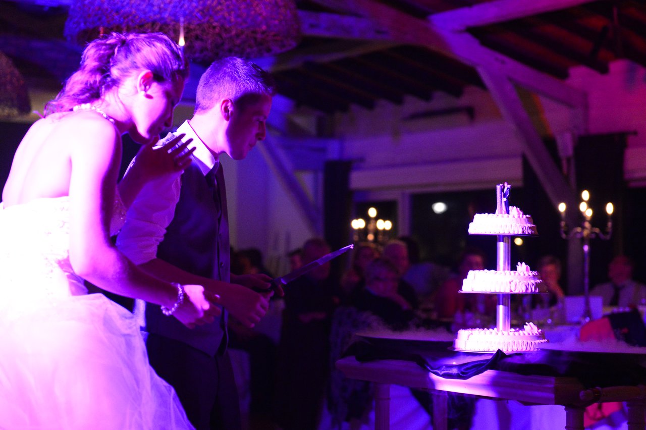 A bride and groom prepare to cut their wedding cake at a reception with guests watching.