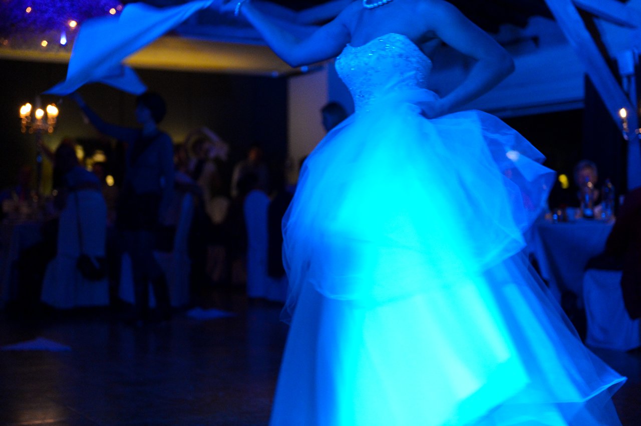 A bride in a white gown dances at a wedding reception, illuminated by blue lighting.