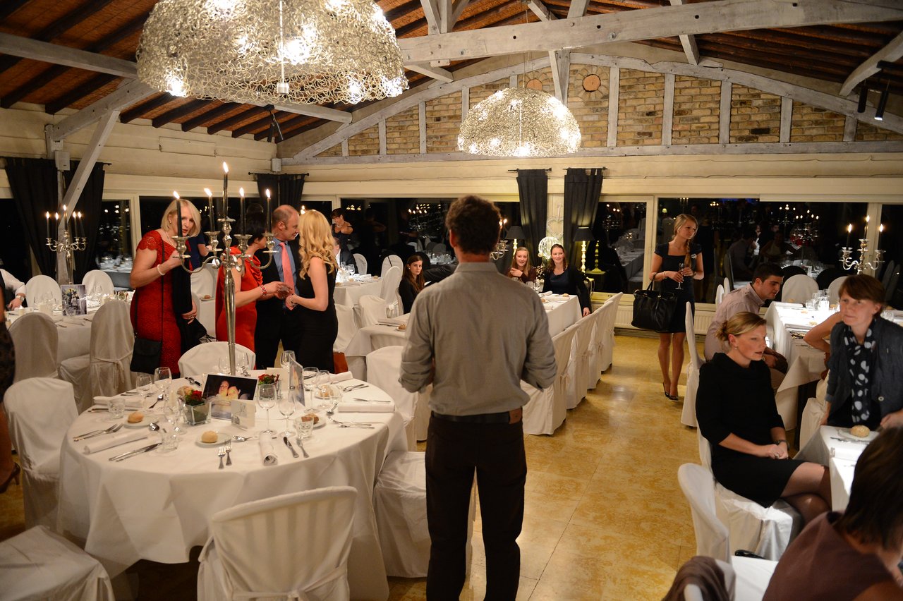 Guests in formal attire are mingling and chatting at a wedding reception in a decorated venue with candlelit tables.