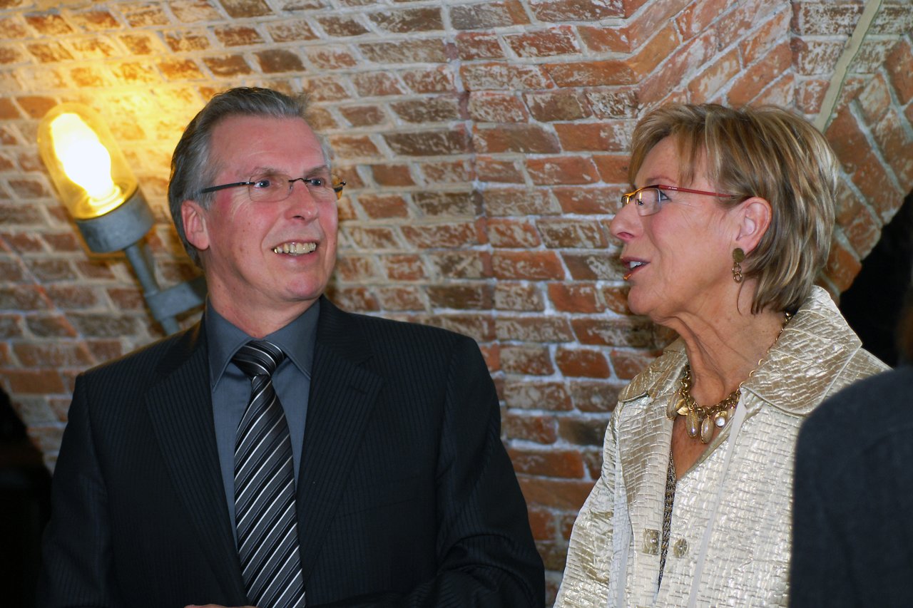A man and a woman in formal attire are smiling and talking at a wedding reception.