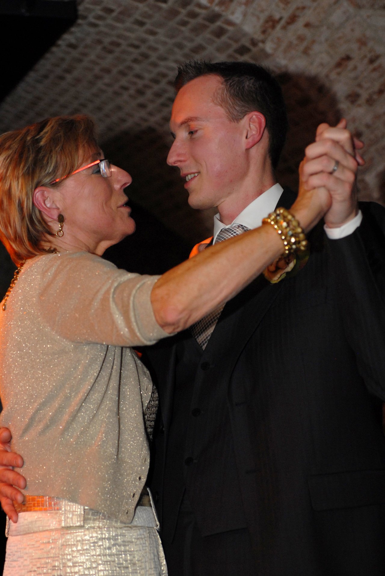 A groom in a suit dances with an older woman at a wedding reception, holding hands and smiling.