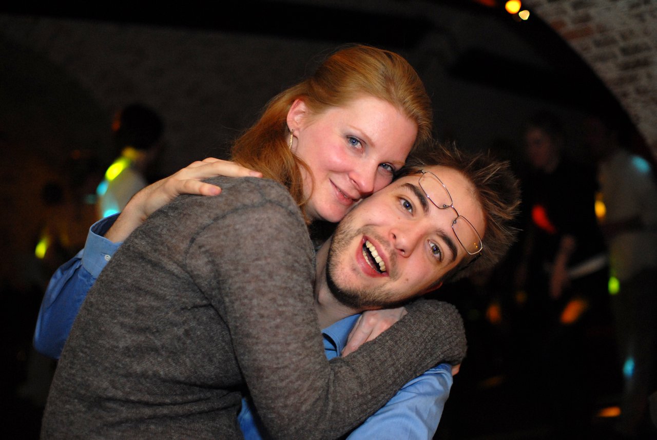 A smiling couple embraces closely at a wedding celebration, looking happy and joyful.