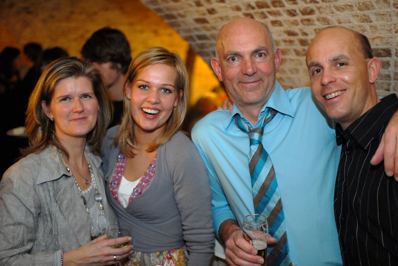 Four people smiling and posing together at a wedding celebration, holding drinks and dressed in semi-formal attire.