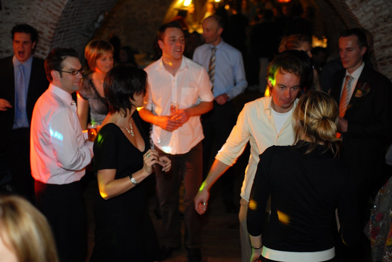 Wedding guests dance and socialize in a dimly lit venue, enjoying the celebration.