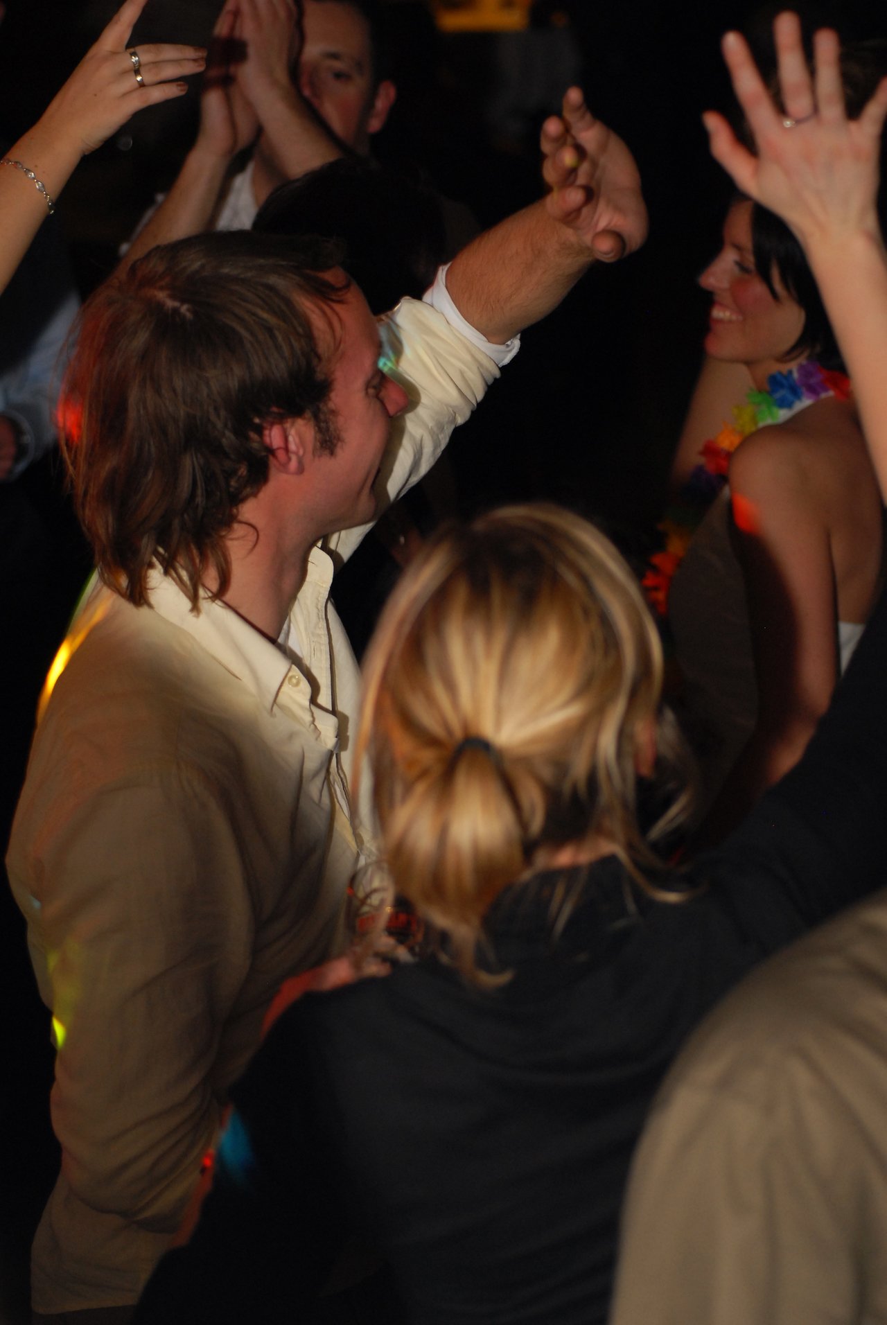 People dancing and celebrating at a wedding reception, with the bride smiling in the background.