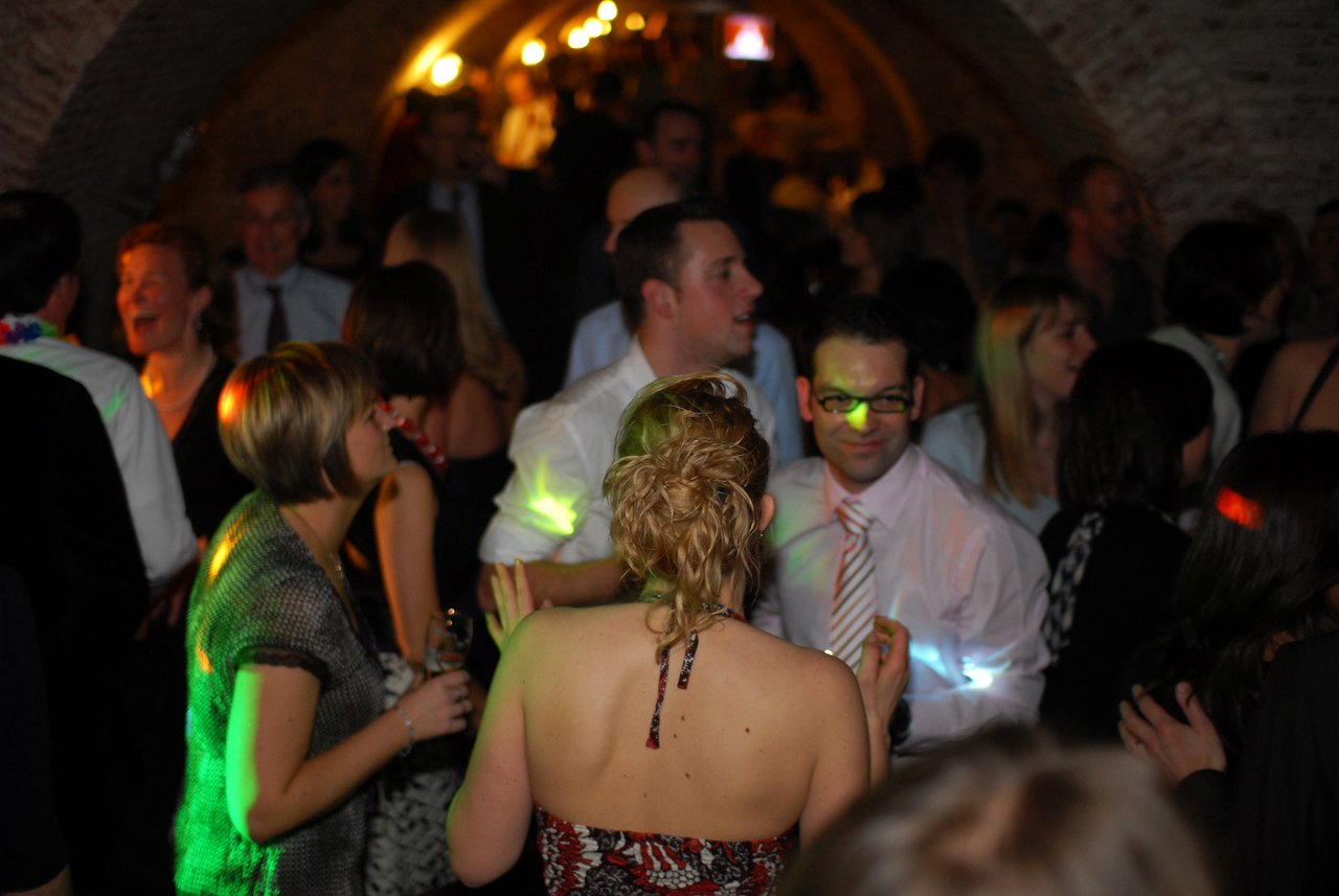 Guests dancing and socializing at a wedding reception in a dimly lit venue with colorful lights.