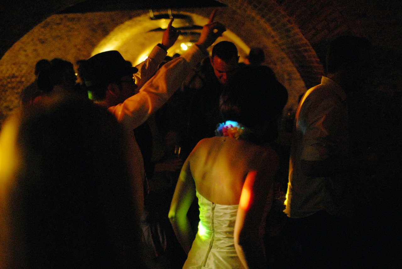 The bride and guests dance in a dimly lit wedding reception, with colorful lights reflecting on their clothing.