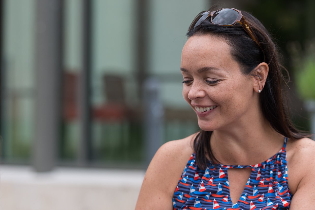 A woman in a colorful dress smiles while looking down at something outside the frame.