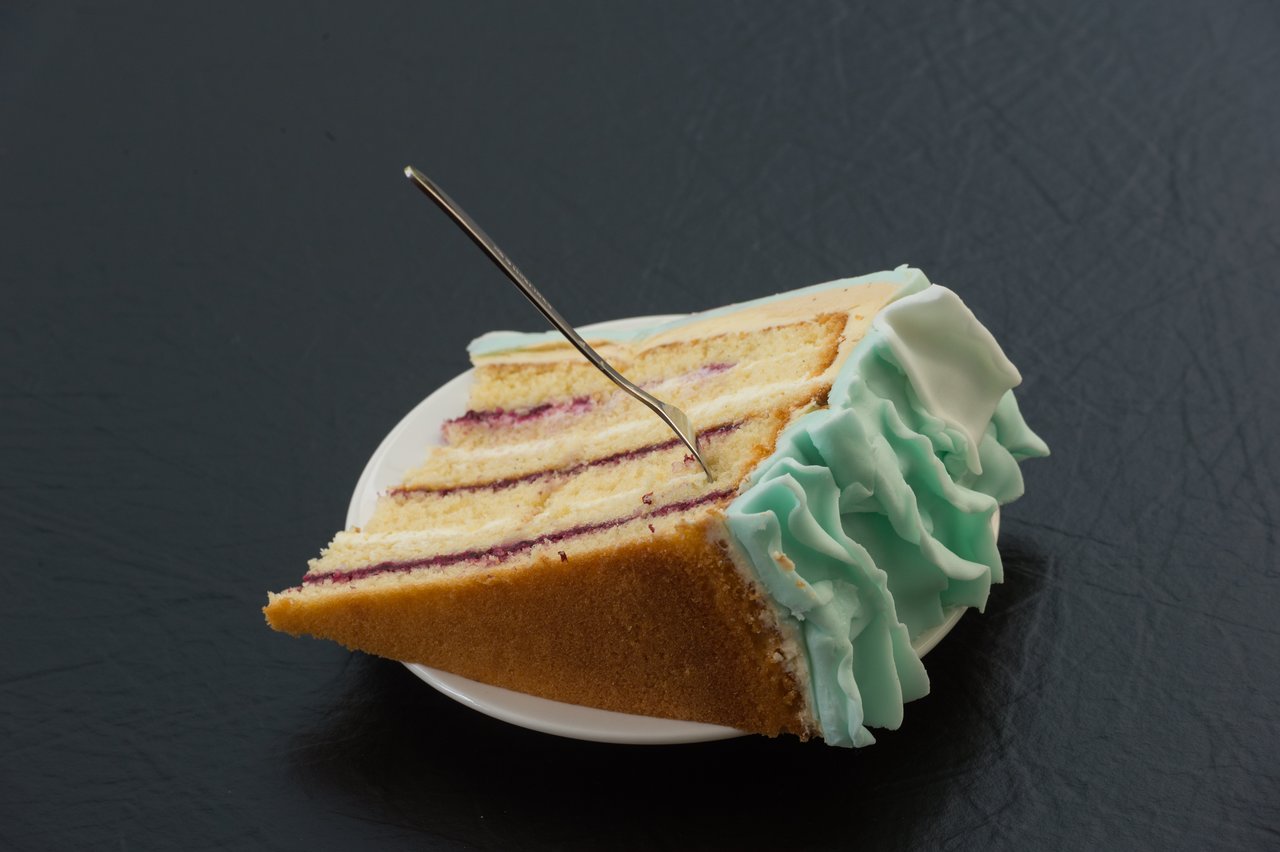 A slice of wedding cake with blue icing and a fork stuck in it on a white plate.