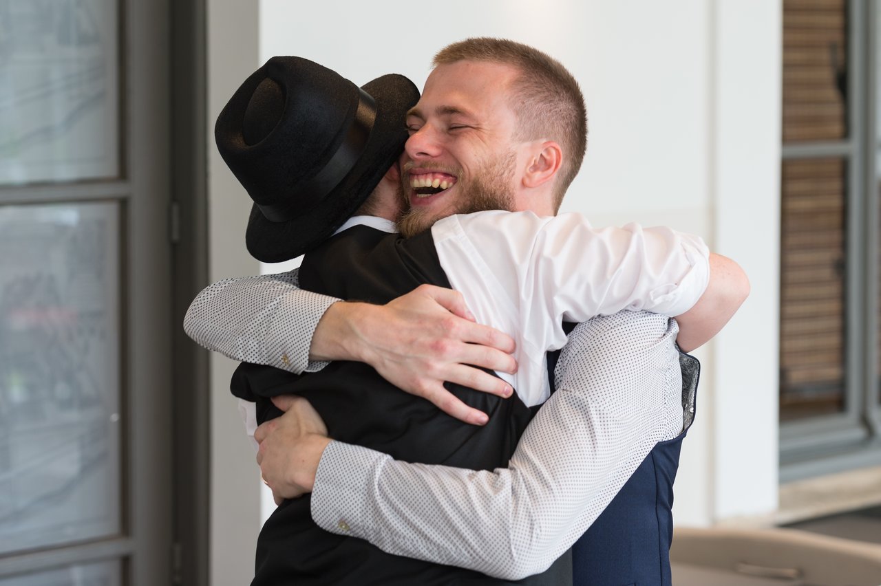 Two men in formal attire share a joyful hug at a wedding celebration.