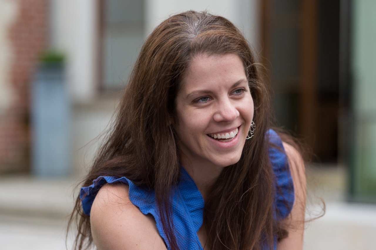 A woman in a blue dress smiles while looking off to the side at a wedding event.