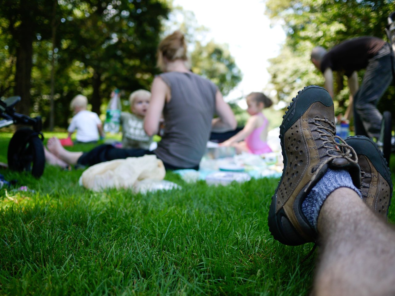 A person relaxes on the grass while a group of people, including children, have a picnic in the background.