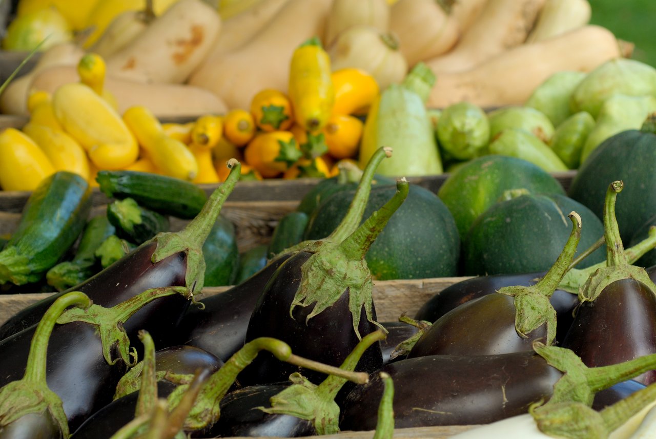 Fresh vegetables, including eggplants, zucchini, and squash, displayed in wooden crates at a farmers market.