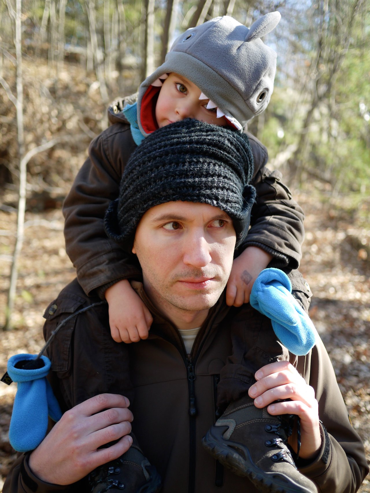 A man carries a child on his shoulders in a wooded area.