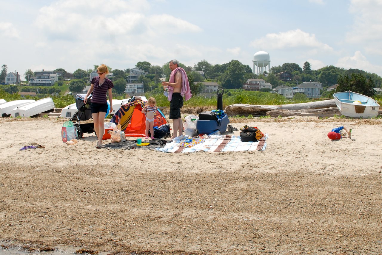 A family sets up a beach picnic with blankets, toys, and a small tent while enjoying a sunny day.