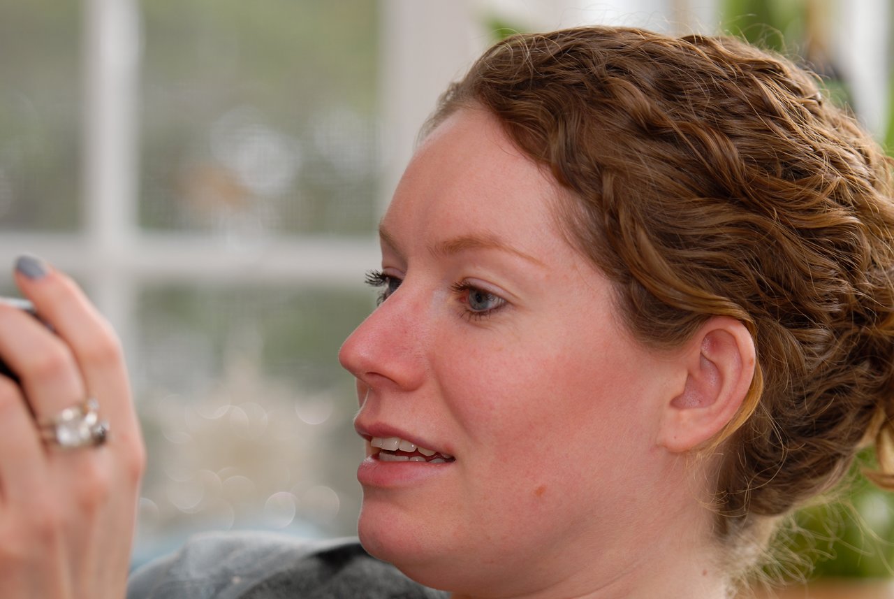 A woman with curly hair looks at an object in her hand with a focused expression.
