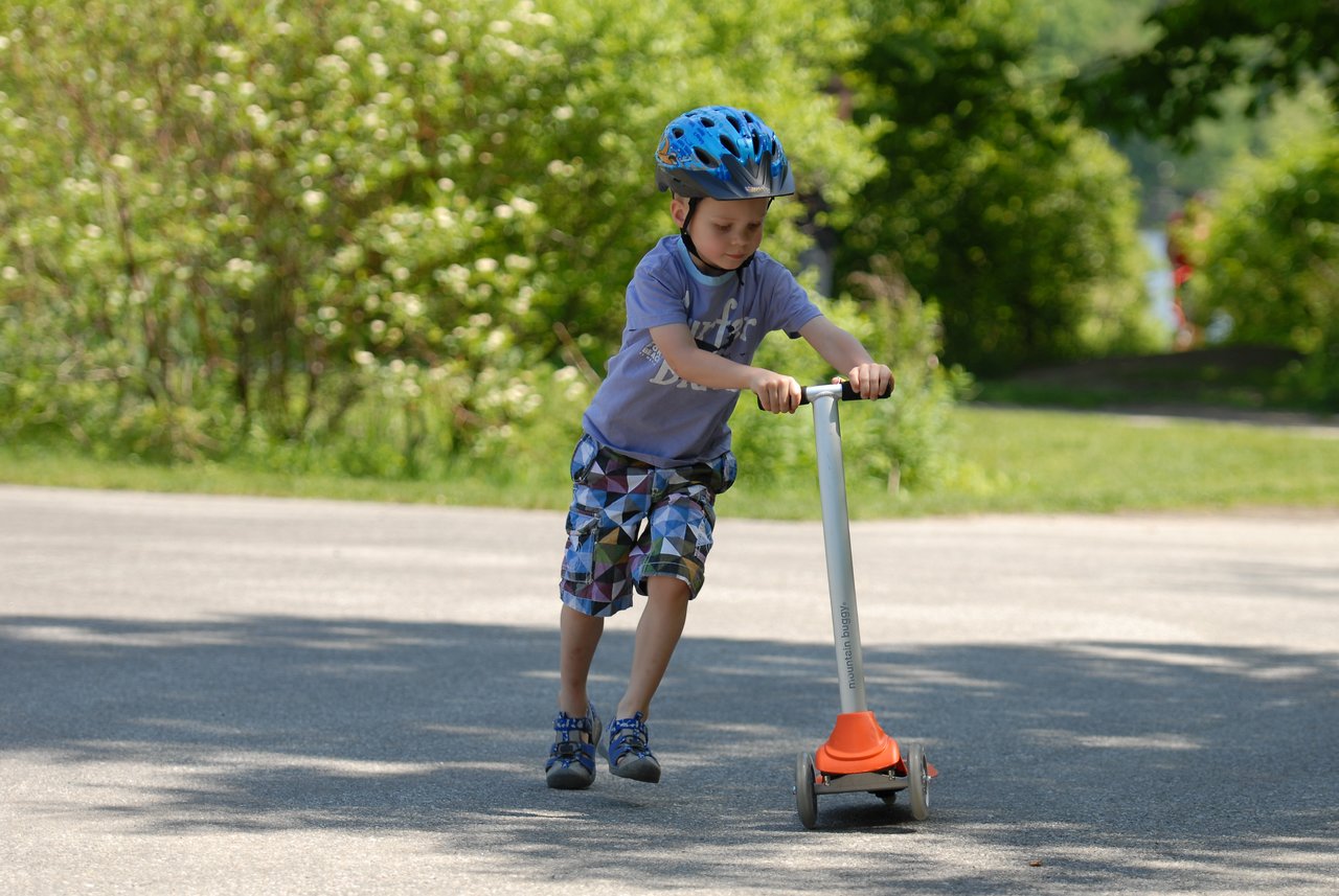 A young child wearing a helmet rides a scooter on a paved path during daytime.
