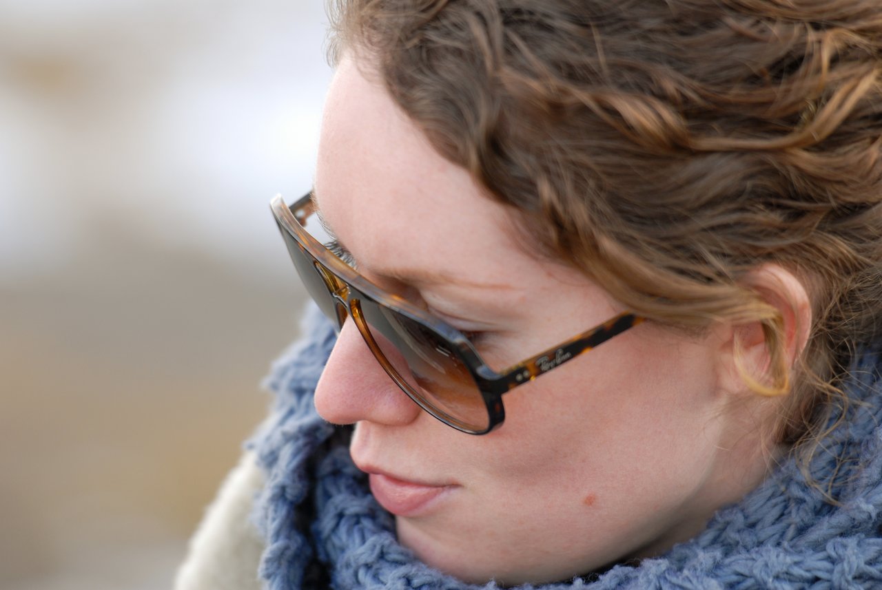 Close-up of a person wearing sunglasses and a blue scarf, looking downward with a neutral expression.