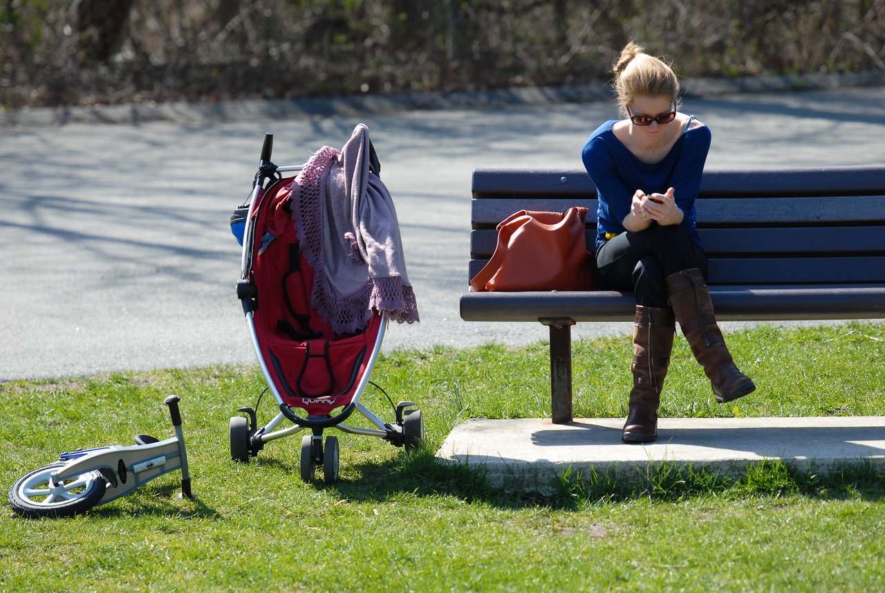 A woman sits on a bench, looking at her phone.