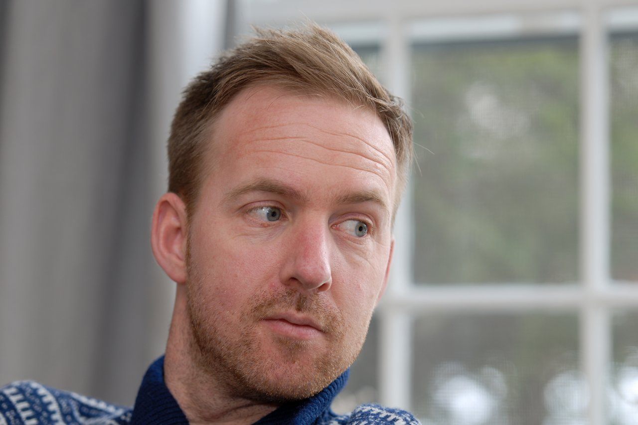 A man with short, light brown hair looks to the side with a neutral expression.