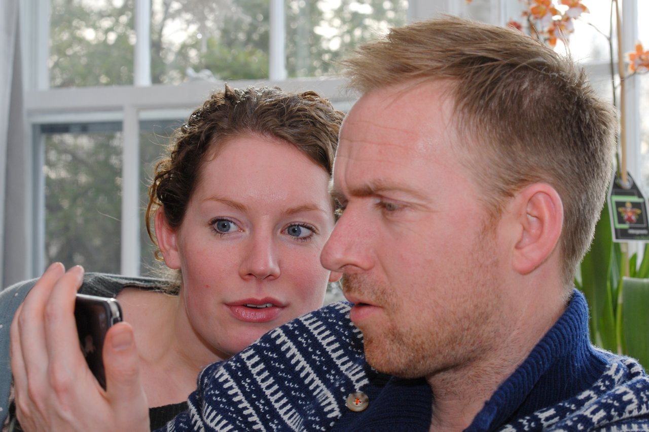 A man and woman closely look at a smartphone screen, appearing focused and engaged in conversation.