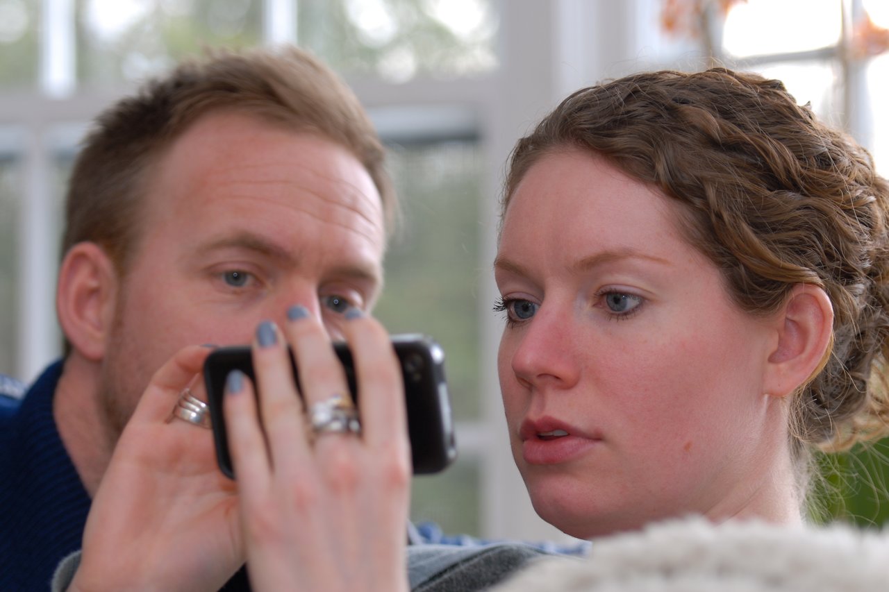 A man and a woman closely look at a smartphone screen, with the woman holding the device.