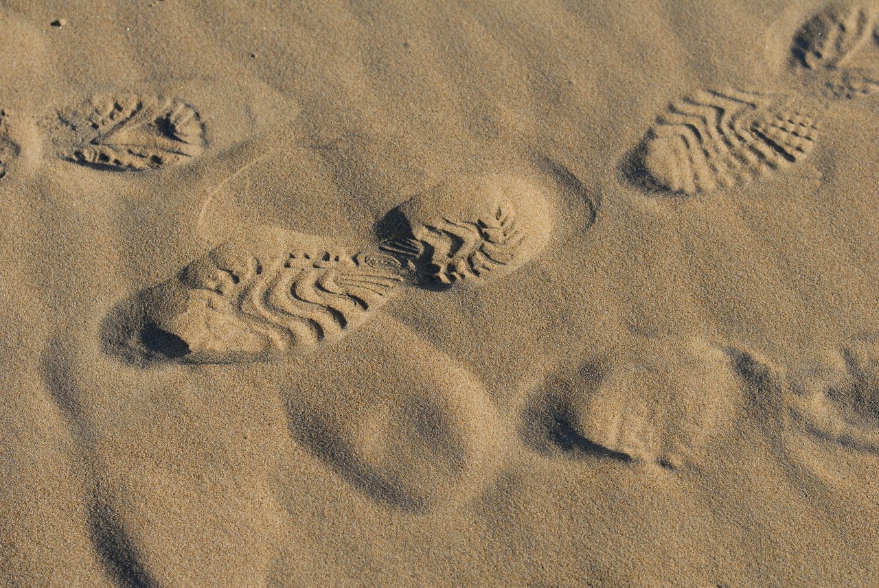 Shoe prints in the sand, partially covered by wind-blown grains.