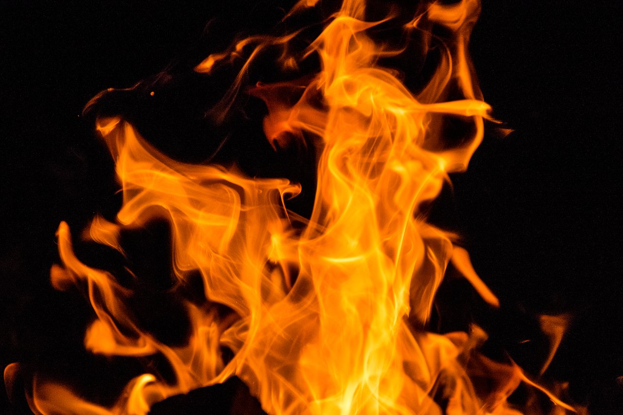 Bright orange flames rise from a campfire at night, creating a warm glow in the darkness.