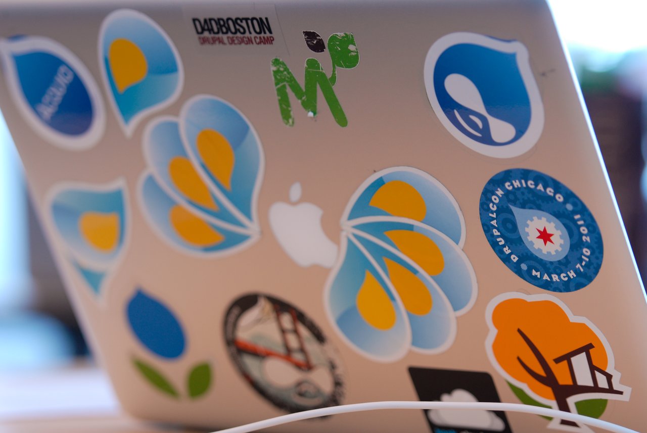 A laptop covered in colorful stickers, including Drupal and tech-related designs, sits on a table during a sprint.