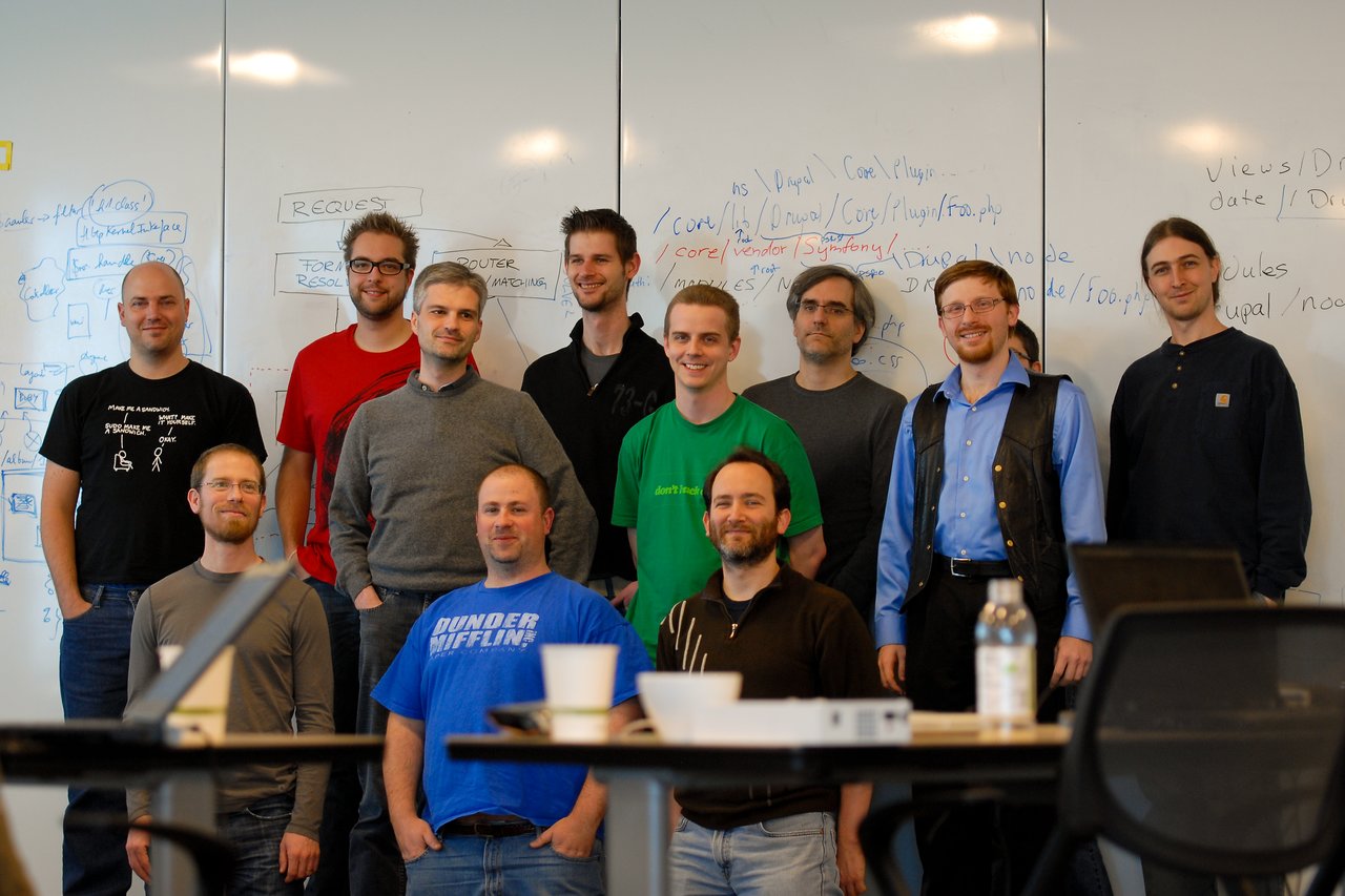 A group of eleven people poses in front of a whiteboard covered with notes and diagrams during a sprint event.