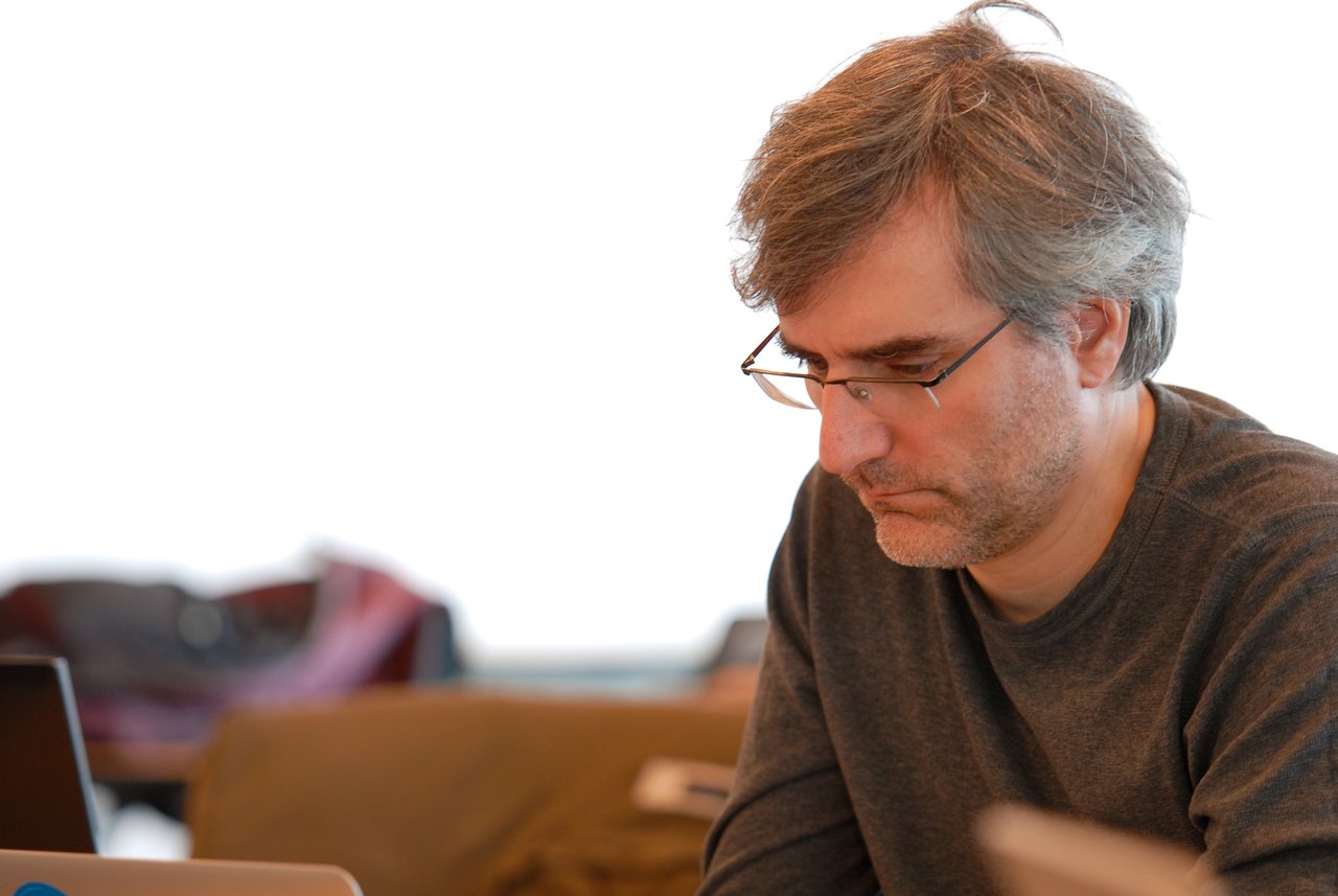 A person wearing glasses and a dark shirt is focused on working at a laptop during a sprint event.