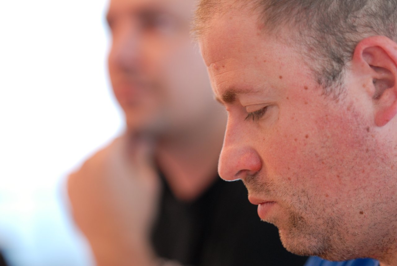 A man in the foreground is focused, while another person in the background appears to be listening or thinking.