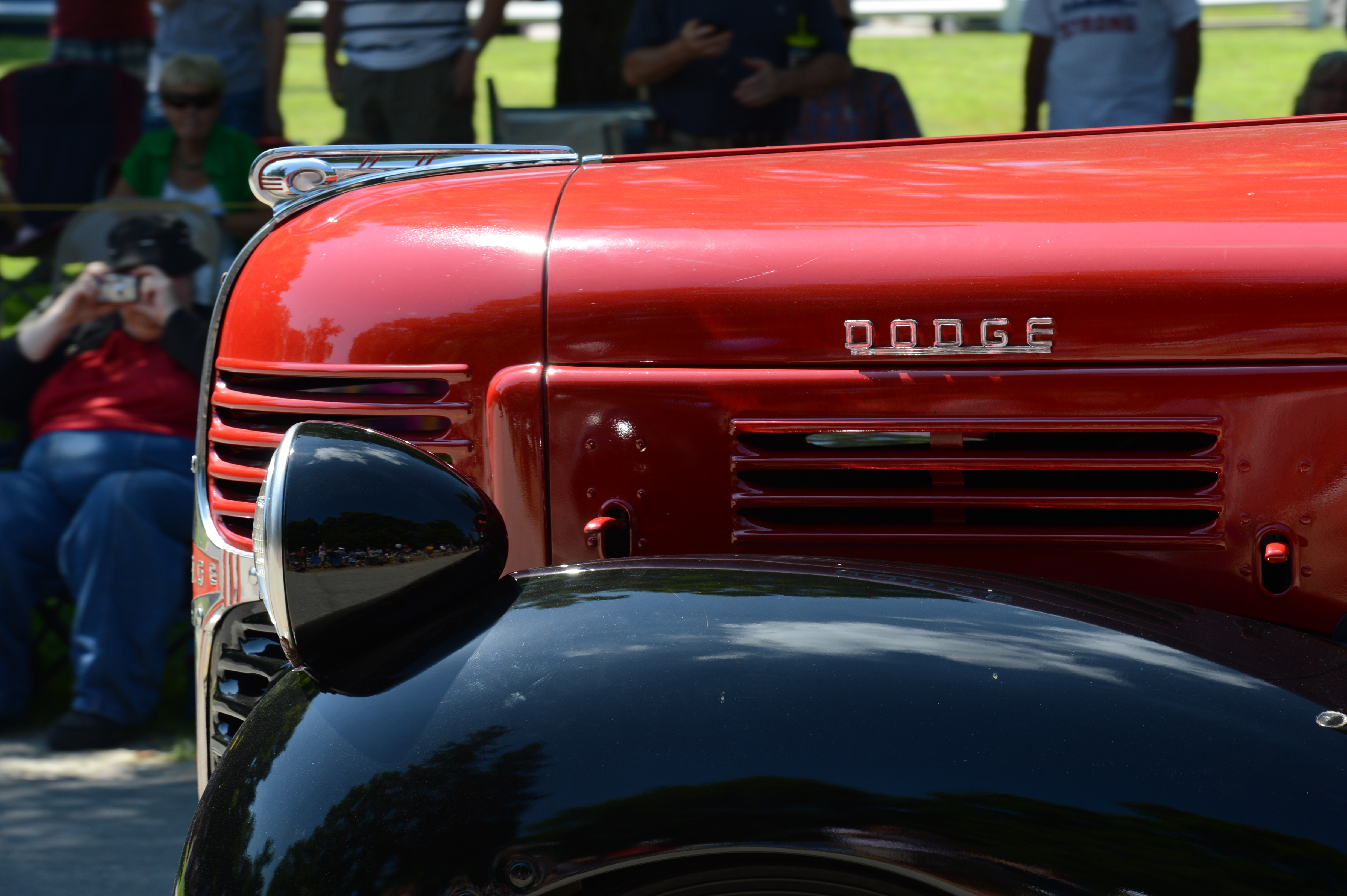 Close-up of a vintage red and black Dodge truck in a parade, with spectators watching and taking photos.