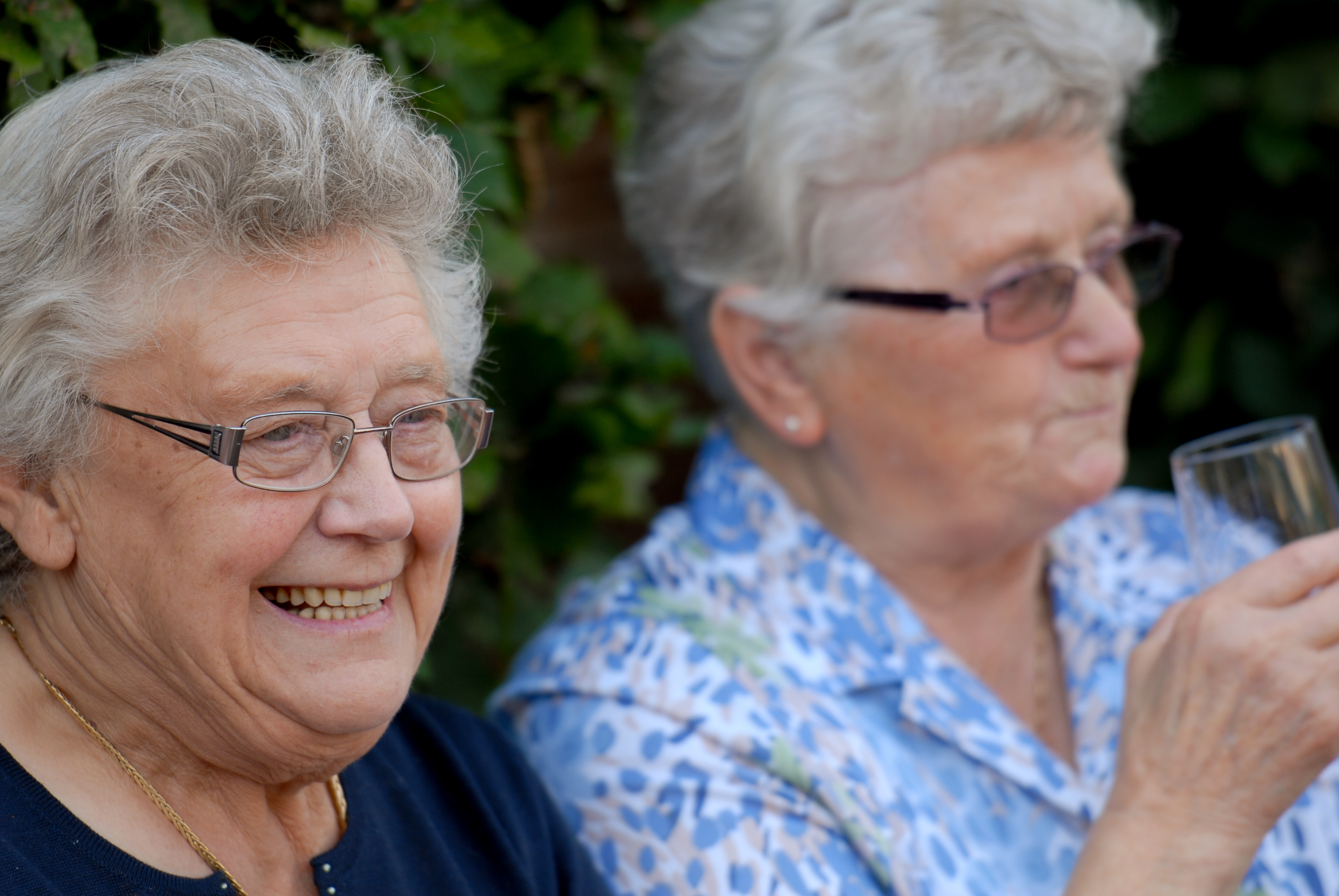 Two elderly women at a party, one smiling and the other holding a glass while looking to the side.