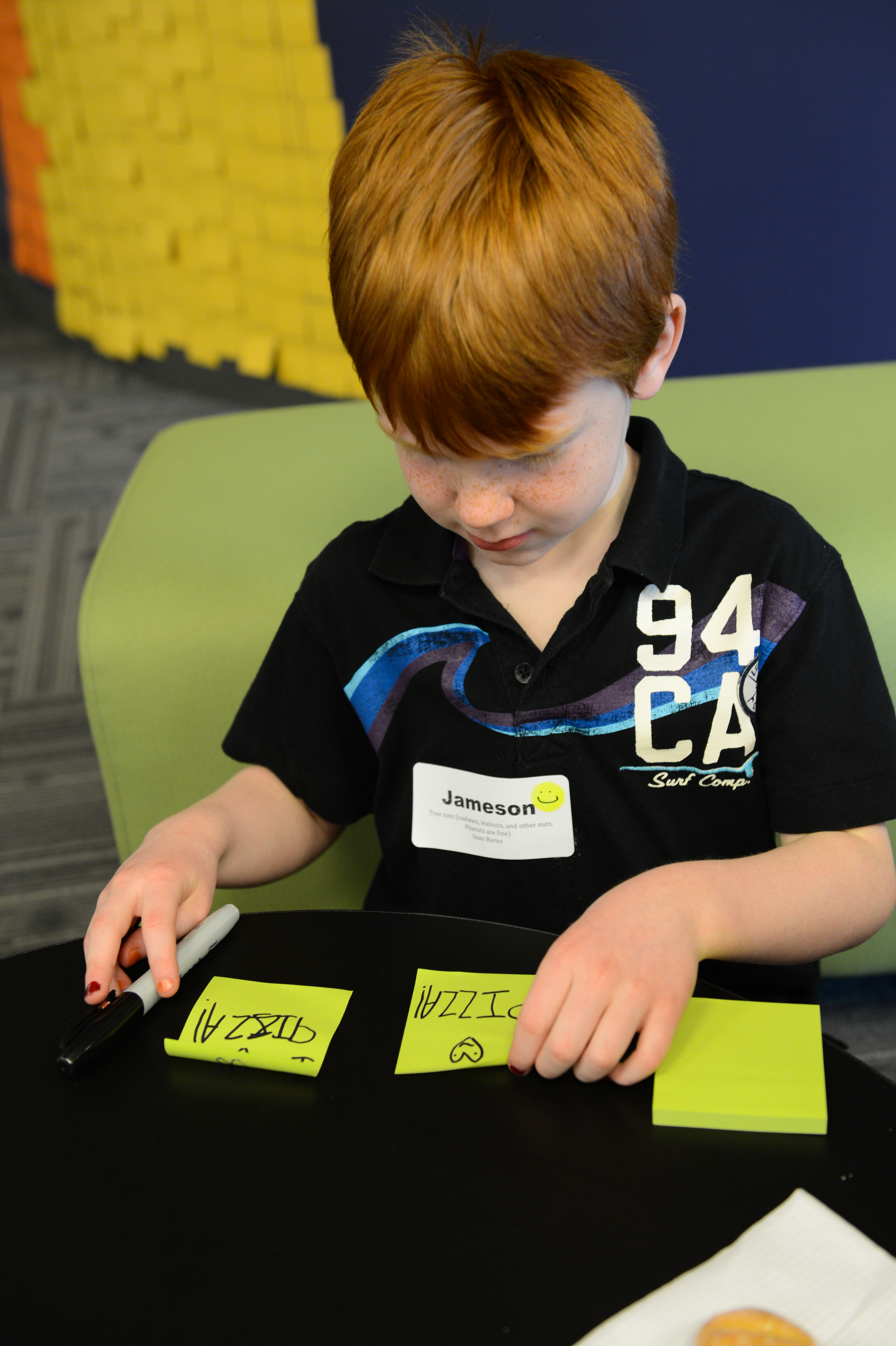A child writes on sticky notes with a marker while sitting at a table.