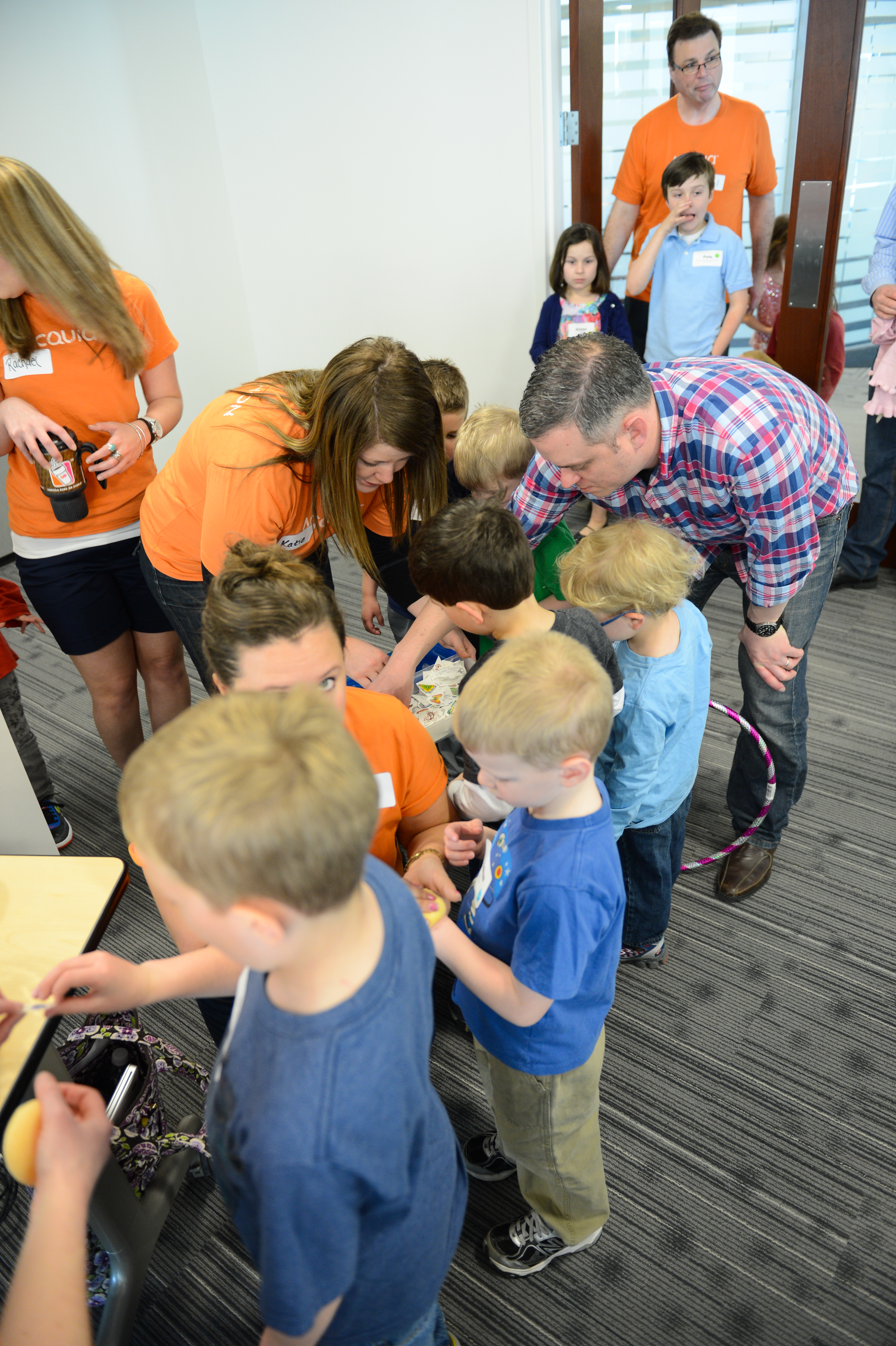 Children and adults gather around a table, engaging in an activity during a "Bring Your Kids to Work" event.