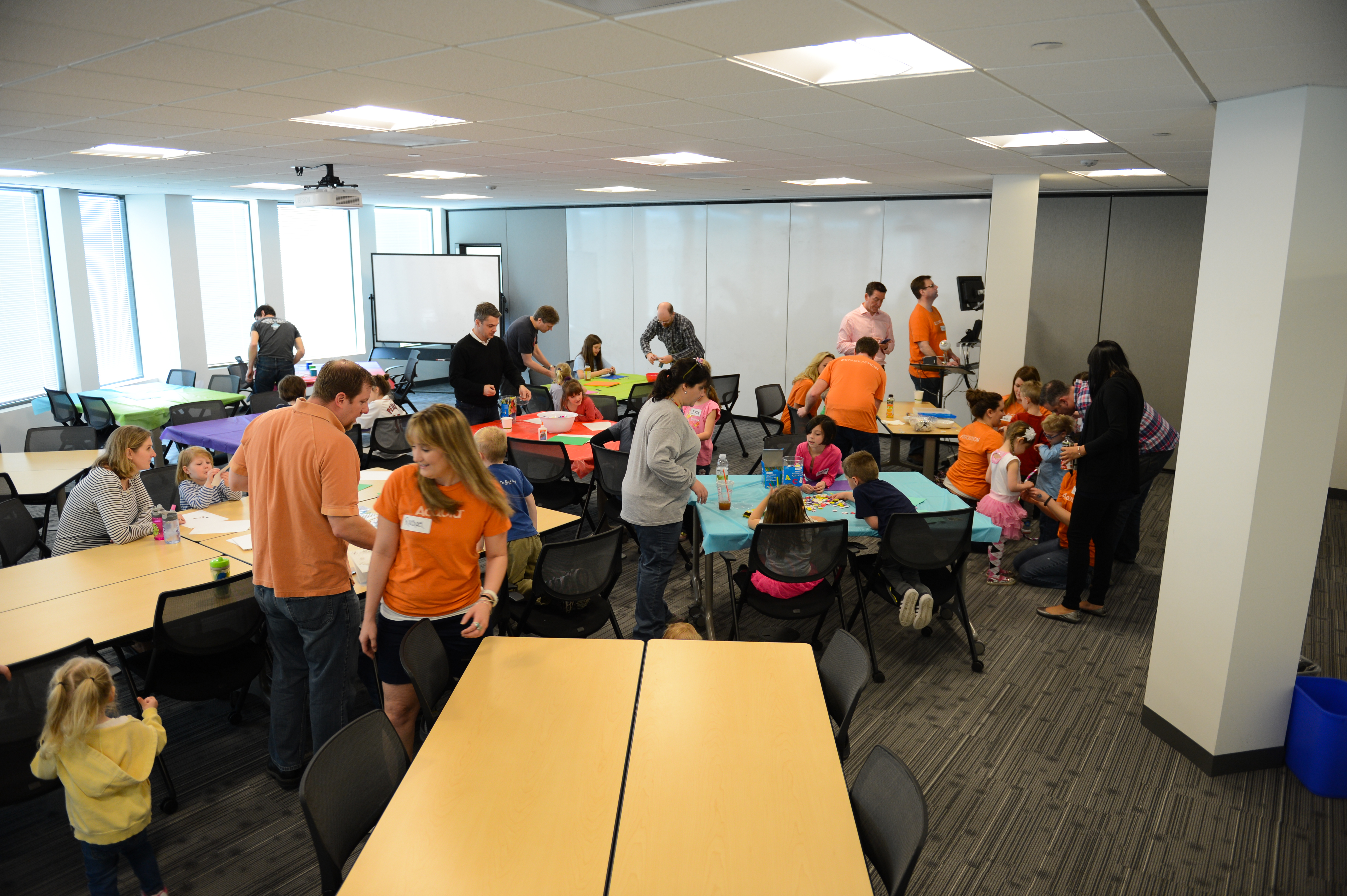 Adults and children participate in arts and crafts activities at a workplace event in a conference room.